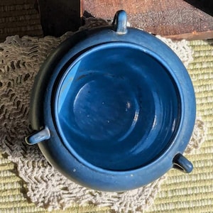 May include: A deep blue ceramic bowl with a rounded shape and three handles. The bowl is empty and has a glossy finish.