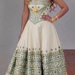 Puede incluir: Vestido largo sin tirantes en color marfil con patrones geométricos verdes. El vestido presenta un corpiño ajustado y una falda amplia. Un collar y pulseras doradas completan el look. Adecuado para ocasiones especiales.