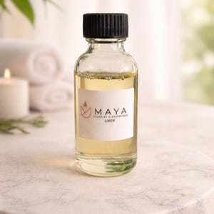 Könnte beinhalten: Eine transparente Glasflasche mit schwarzem Verschluss, gefüllt mit einer hellgelben Flüssigkeit. Auf dem weißen Etikett steht "MAYA CANDLES & ESSENTIALS LINEN". Die Flasche steht auf einer Marmoroberfläche.