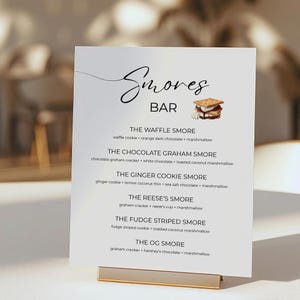 May include: A white sign with black text listing different s'mores variations. The sign reads "Smores Bar" and lists the ingredients for each s'more, such as "The Waffle Smore: waffle cookie, orange dark chocolate, marshmallow".