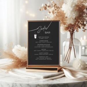 May include: A black chalkboard sign with a gold frame and stand, listing a menu of soda bar drinks with names like "Dirty Dr. Pepper", "Cherry Bomb", and "Watermelon Sugar".