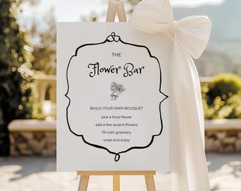 May include: A white sign on a wooden easel with the text "The Flower Bar" in elegant script. The sign includes instructions for building a bouquet. A large white bow and fabric drape the side.