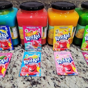 Pode incluir: Quatro frascos quadrados grandes de plástico cheios de líquido azul, vermelho, laranja e verde, cada um com uma tampa preta. Oito pacotes de mistura para bebida Kool-Aid estão dispostos à frente, com sabores como framboesa azul.