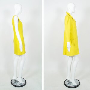 May include: A yellow sleeveless dress and a yellow coat with a collar and buttons. Both garments are on mannequins with white skin.