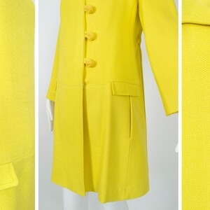 May include: A bright yellow coat with a long, straight silhouette and a row of large, yellow, rose-shaped buttons.