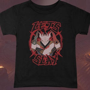 May include: Black t-shirt featuring a graphic of a warrior with two swords and the words "LET'S SLAY" in red. The warrior has a white head and is wearing a brown and tan outfit. The design is set against a red circular background.