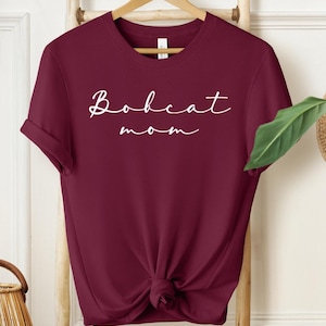 May include: Burgundy t-shirt with white text that reads "Bobcat mom".