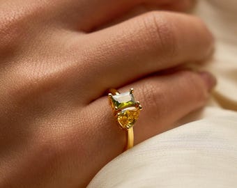 Könnte beinhalten: Ein goldener Ring mit einem rechteckigen, hellgrünen Edelstein und zwei kleineren gelben Edelsteinen. Der Ring hat ein zartes Goldband. Der Ring ist ein Schmuckstück.