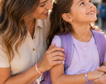 Könnte beinhalten: Drei Perlenarmbänder mit kleinen Herzanhängern, getragen von zwei Erwachsenen und einem Kind. Die Armbänder bestehen aus bunten Perlen in Pink, Lila und Türkis, die jeweils mit einem metallischen, herzförmigen Anhänger verziert sind.