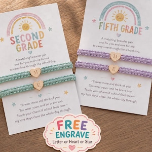 May include: Two sets of matching woven bracelets on display cards. One set is light green, the other is light purple. Each bracelet features a small gold heart charm engraved with letters. The cards display rainbow graphics and text including SECOND GRADE and FIFTH GRADE, plus a small sign stating FREE ENGRAVE Letter or Heart or Star.