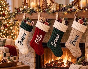 Könnte beinhalten: Vier Weihnachtssocken aus Zopfstrick hängen in einer Reihe. Die erste ist cremefarben mit dunkelgrünem Umschlag und dem Namen Juniper. Die zweite ist rot mit cremefarbenem Umschlag und dem Namen Milo. Die dritte ist dunkelgrün mit cremefarbenem Umschlag und dem Namen Sienna. Die vierte ist beige mit cremefarbenem Umschlag und dem Namen Beau.