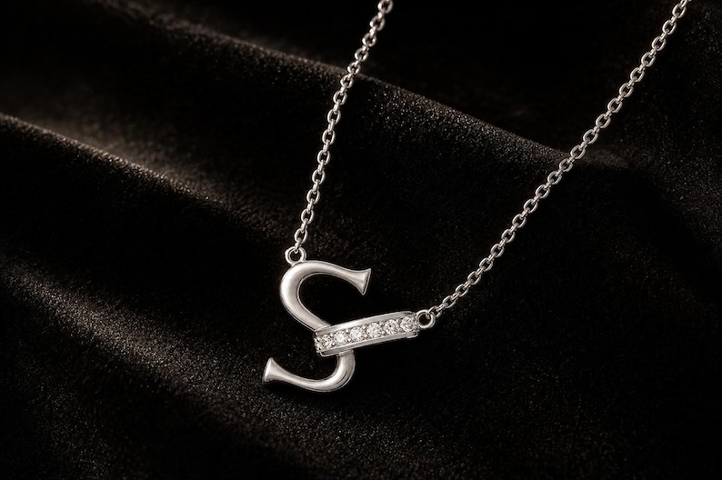 Pu&ograve; includere: Una collana color argento con un ciondolo a forma di lettera S. La lettera &egrave; impreziosita da una barra orizzontale incastonata con sei piccole pietre rotonde e trasparenti. Il ciondolo &egrave; fissato a una sottile catenina color argento a maglie.