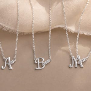 Pu&ograve; includere: Tre collane color argento con le lettere A, B e M come ciondoli. Ogni lettera &egrave; attaccata a una sottile catena d'argento ed &egrave; accentuata da una piccola barra rettangolare incastonata con minuscole pietre chiare e scintillanti posizionate in diagonale.