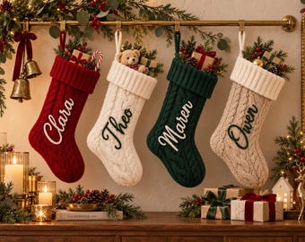 Könnte beinhalten: Vier Weihnachtsstrümpfe aus Zopfstrick hängen an einer goldenen Stange. Die Strümpfe sind rot, weiß, dunkelgrün und beige, jeder mit einem weiß oder dunkelgrün gestickten Namen: Clara, Theo, Maren und Owen. Jeder Strumpf ist mit Tannengrün gefüllt.