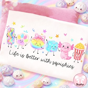 May include: A white t-shirt featuring a colourful graphic of six cartoon characters including a butter stick, paw, bow, ice cube, axolotl, and popcorn bucket, with the text "Life is better with squishies" printed in black cursive script below.