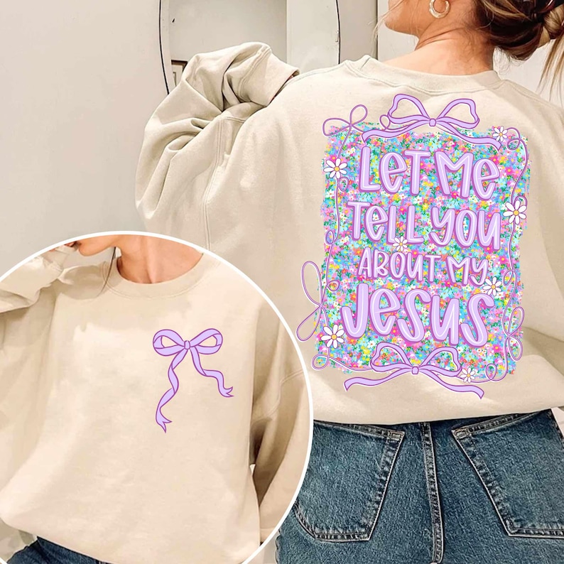 Puede incluir: Una sudadera beige con un dise&ntilde;o floral y el texto "Let Me Tell You About My Jesus" en la espalda. La parte delantera de la sudadera tiene un lazo morado.