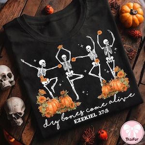 May include: Black t-shirt featuring a design of dancing skeletons with sunflowers and pumpkins. The phrase "dry bones come alive" and the Bible verse Ezekiel 37:5 are printed on the shirt. A Halloween-themed design.