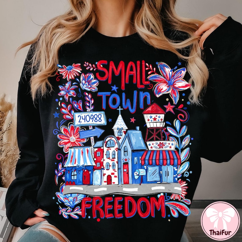 May include: Black sweatshirt with a colorful graphic of a small town scene. The design includes buildings, flowers, and the words "SMALL TOWN FREEDOM" in red and blue. A postal code is also included.