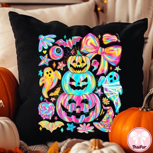 May include: Black decorative pillow with a colorful Halloween design. The design features stacked jack-o'-lanterns, ghosts, bats, bows, and stars in vibrant rainbow hues. The pillow is surrounded by pumpkins.
