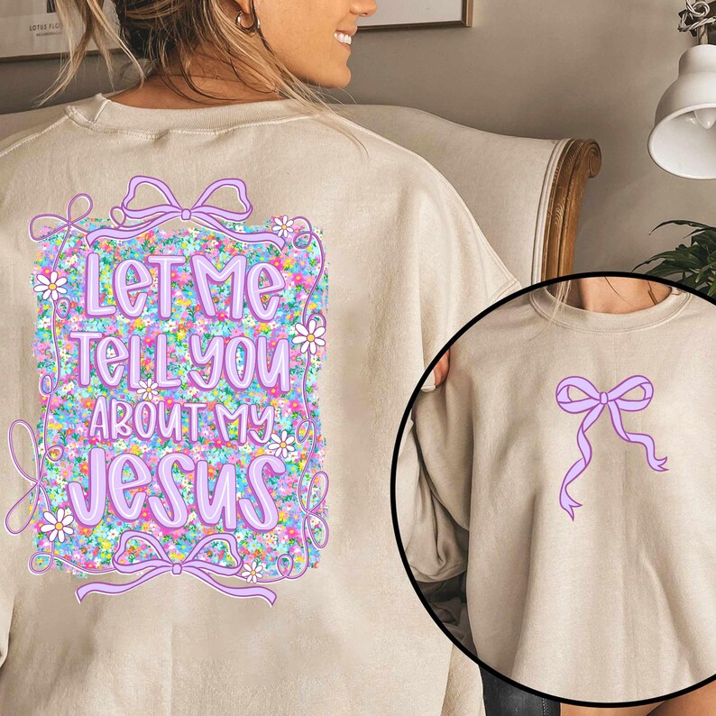 Puede incluir: Una sudadera beige con un dise&ntilde;o floral y el texto "Let me tell you about my Jesus" impreso en la espalda. La parte delantera de la sudadera tiene un lazo morado.