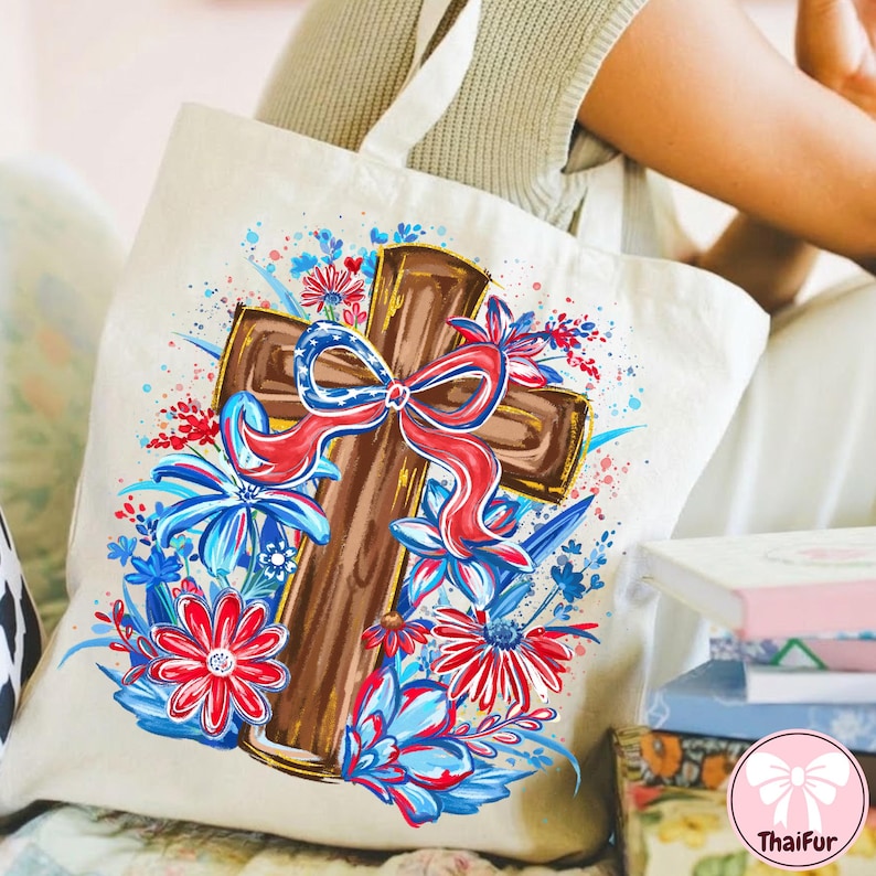 May include: Cream-colored tote bag featuring a brown cross adorned with a red, white, and blue bow and floral accents. The design includes red and blue flowers and leaves, creating a patriotic and decorative theme.