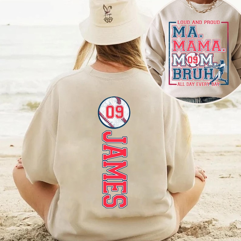 May include: Tan sweatshirt with a baseball graphic and the number 09. The text "JAMES" is printed vertically below the baseball. The sweatshirt is being worn by a person sitting on a beach.