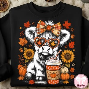 Può includere: Una felpa nera con la grafica di una soffice mucca Highland bianca che indossa un fiocco a quadri e occhiali a forma di cuore. La mucca è accanto a una tazza di caffè, girasoli, zucche e foglie autunnali. Il testo ThaiFur è nell'angolo in basso.