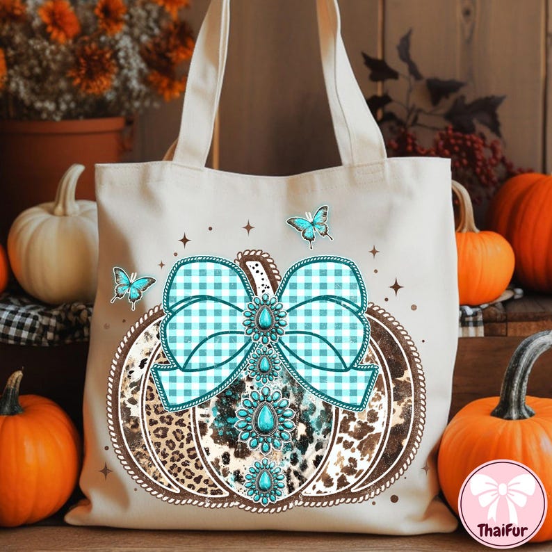 May include: Beige tote bag featuring a pumpkin design with a turquoise gingham bow and turquoise gemstone accents. The pumpkin has a leopard print pattern and is surrounded by butterflies. Perfect for fall.