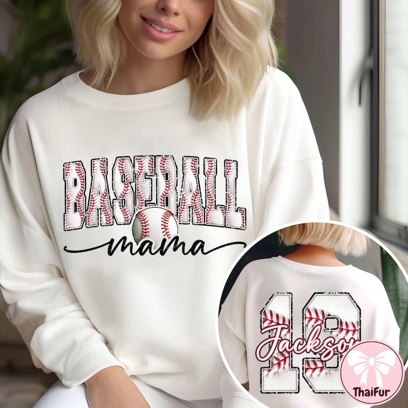 May include: Cream sweatshirt featuring the text "BASEBALL mama" in a baseball-themed design. The word "BASEBALL" is in a block letter style with red baseball stitching. A baseball graphic is centered below the word. The back has the number 19 and the name "Jackson".