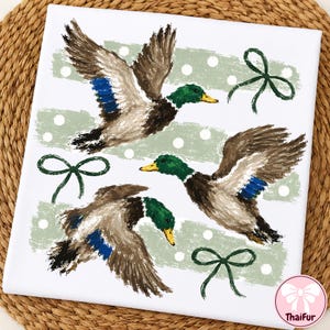 Pu&ograve; includere: Un quadrato di tessuto bianco con un motivo stampato di tre germani reali in volo con piumaggio marrone, verde e blu. Il design include strisce orizzontali a pennellate verde salvia con pois bianchi e fiocchi disegnati a tratto verde scuro.