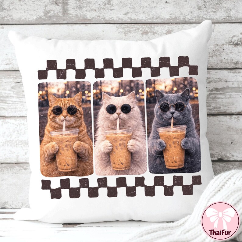 May include: White throw pillow featuring three cats wearing sunglasses and drinking iced coffee. The cats are a ginger tabby, a white cat, and a gray cat. The pillow has a brown and white checkered border.
