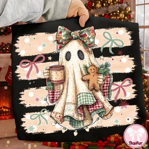 May include: A black fabric item featuring a graphic of a ghost wearing a floral bow, holding a mug and a gingerbread man. The design includes horizontal beige brushstrokes, pink bows, green pine sprigs, and string lights against a black background.