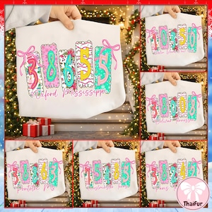 Może przedstawiać: Biała torba typu tote z kolorowym wzorem przedstawiającym liczby 38655, zaakcentowanym różowymi kokardkami i napisem "Oxford, Mississippi". Liczby mają kwiatowe i wzorzyste detale. Torba jest trzymana przez osobę.