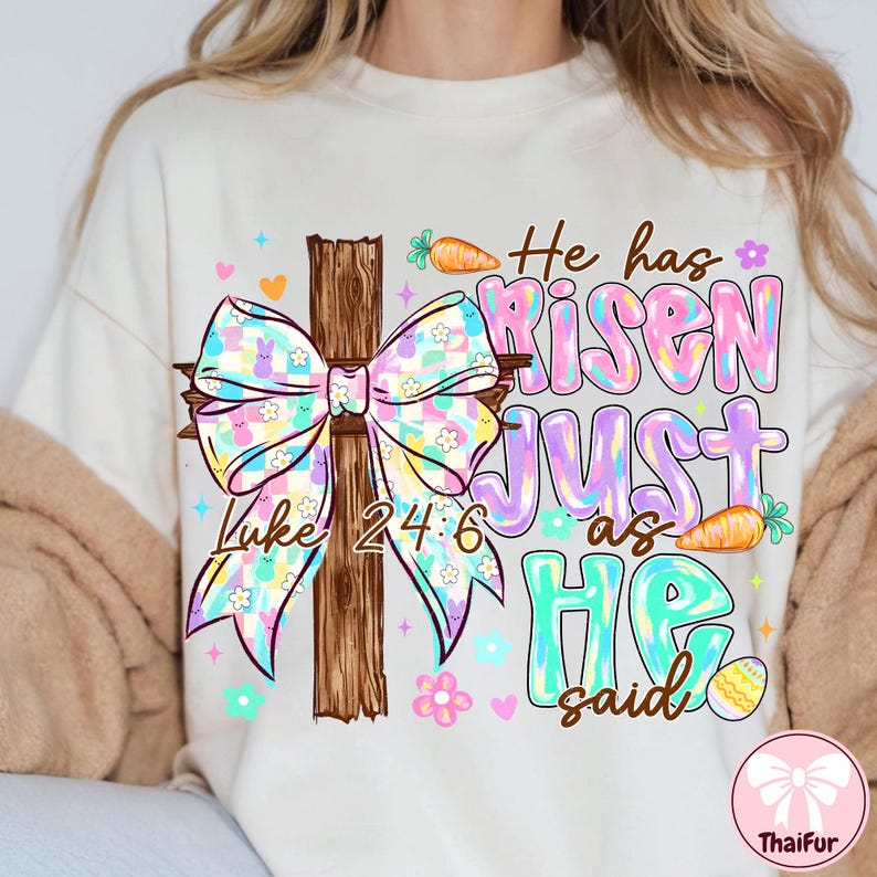 May include: Cream-colored t-shirt with a colorful Easter-themed graphic. The design features a wooden cross with a pastel bow, the text "He has Risen Just as He said" and the Bible verse Luke 24:6. Includes carrots, flowers, and an Easter egg.