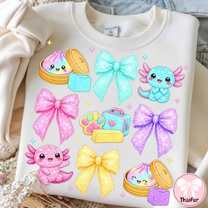 May include: A cream-colored sweatshirt featuring a graphic print of two axolotls, two steamed buns in bamboo baskets, four glittery bows in cyan, pink, purple, and yellow, a paw print, a small suitcase, and small colorful stars.