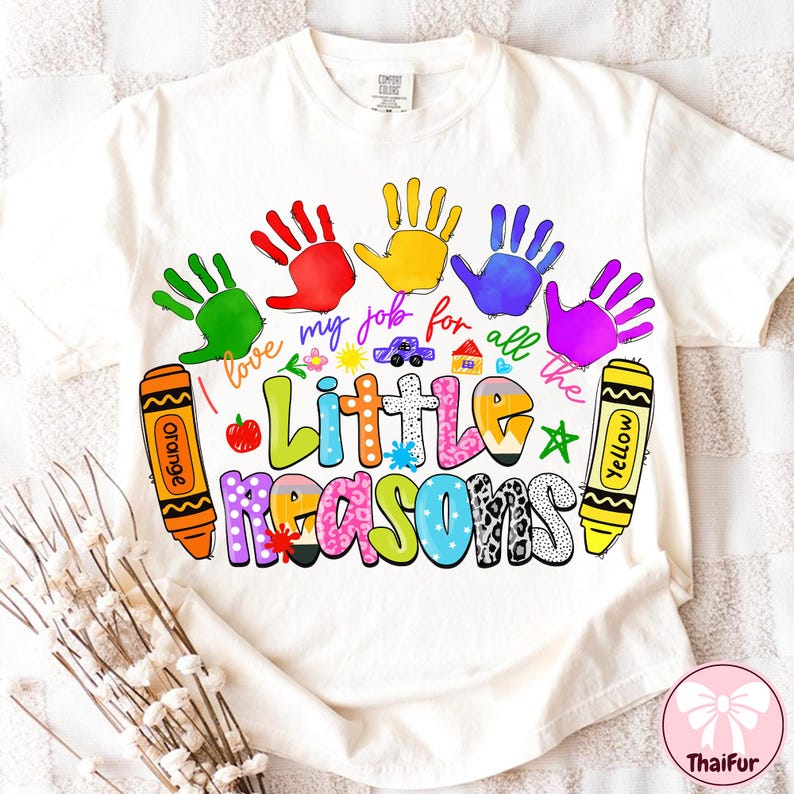 May include: Cream-colored t-shirt with a colorful graphic design. The design includes handprints, crayons, and the text "I love my job for all the Little Reasons." A cute car and house are also included in the design.