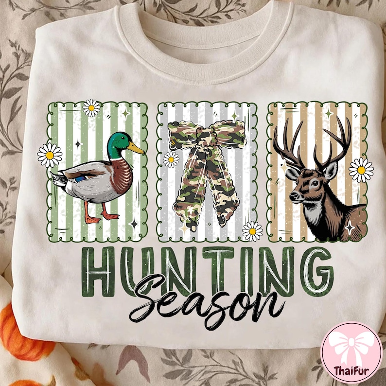 Puede incluir: Sudadera crema con tem&aacute;tica de caza. Presenta un pato, un lazo de camuflaje y un ciervo, cada uno en un dise&ntilde;o enmarcado. Las palabras "HUNTING Season" est&aacute;n impresas en verde y negro. Se incluyen acentos de margaritas.