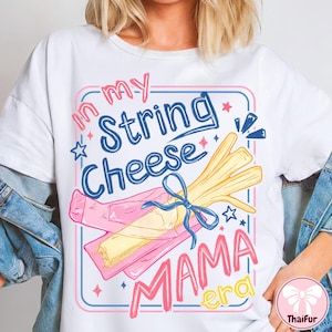 May include: White t-shirt with a colourful graphic design. The design features the text "In my String Cheese Mama Era" in pink and blue, along with an illustration of string cheese and a pink wrapper. The design is framed with a pink and blue border.