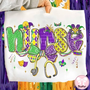 Puede incluir: Sudadera blanca con la palabra "NURSE" en letras grandes y coloridas. Las letras son verdes, moradas y amarillas con purpurina y decoraciones temáticas de Mardi Gras, incluyendo un estetoscopio, un lazo y una máscara. El diseño es festivo y celebratorio.