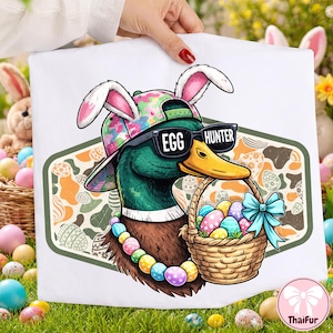 May include: White tote bag with a cartoon duck wearing sunglasses that read "EGG HUNTER" and bunny ears. The duck holds a basket of Easter eggs and wears a colorful beaded necklace. The background has an Easter egg pattern.
