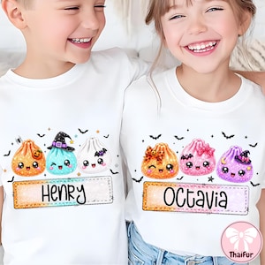 May include: Two white t-shirts featuring colorful, glittery, cartoon-style dumpling characters with faces. The left shirt displays the name Henry, and the right shirt displays the name Octavia. Both designs include small bats, stars, and Halloween motifs.