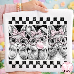 May include: White sweatshirt featuring a black and white checkered border and a triptych of bunny illustrations. Each bunny wears heart-shaped glasses, a pink bow, and has a different expression. One bunny blows a pink bubble.