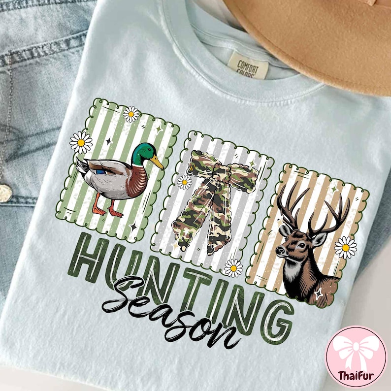 Puede incluir: Camiseta azul claro con un gr&aacute;fico de "Hunting Season". El dise&ntilde;o presenta un pato, un lazo de camuflaje y un ciervo, cada uno dentro de un marco decorativo. La camiseta tiene una etiqueta Comfort Colors.
