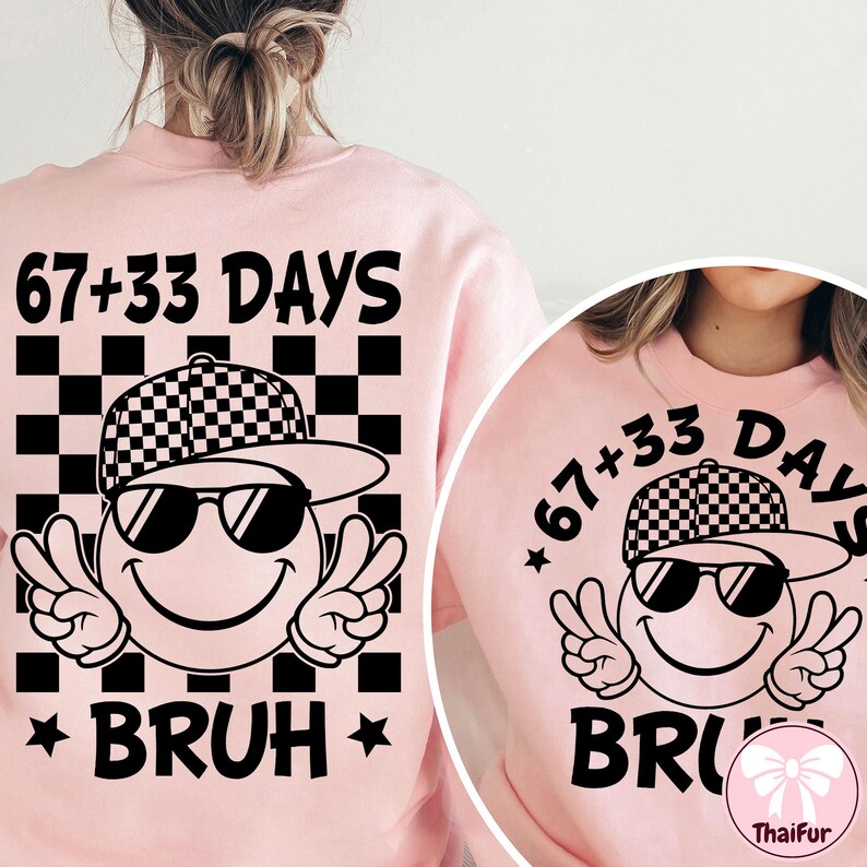 May include: Pink sweatshirt with a graphic featuring a smiley face wearing sunglasses and a checkered hat, with peace signs. The text reads "67+33 DAYS" above and "BRUH" below the graphic.