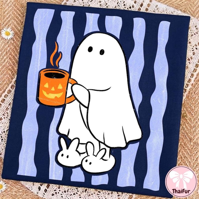 May include: A dark blue t-shirt featuring a white ghost character holding an orange jack-o'-lantern mug with steam rising from it. The ghost wears white bunny slippers. The background of the graphic consists of vertical light blue wavy stripes.