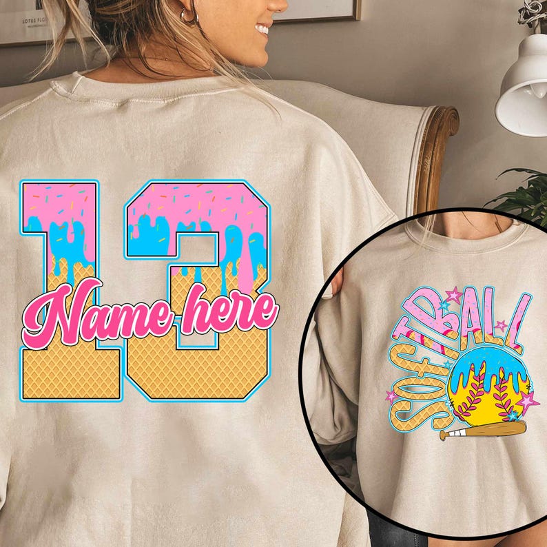 May include: A beige sweatshirt with a pink and blue ice cream cone design with the number 13 and the text "Name here". The back of the sweatshirt has a softball design with the text "Softball".