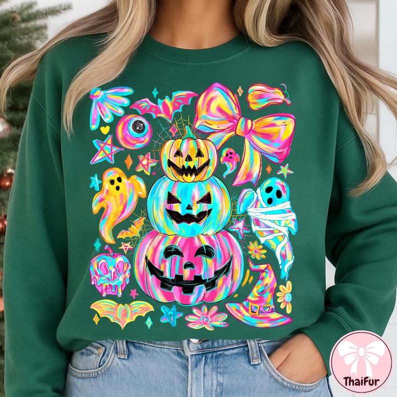 May include: A dark green sweatshirt featuring a colorful Halloween-themed design. The graphic includes stacked jack-o'-lanterns, ghosts, bats, bows, and stars in vibrant rainbow hues. The design is whimsical and festive, perfect for the spooky season.