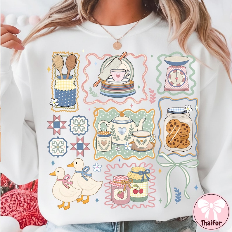 Peut inclure: Sweat-shirt blanc avec un motif color&eacute; illustrant des &eacute;l&eacute;ments de cuisine et de p&acirc;tisserie. Le motif comprend une th&eacute;i&egrave;re, des biscuits, des canards, des pots de confiture et une balance. Le motif est encadr&eacute; de bordures d&eacute;coratives.