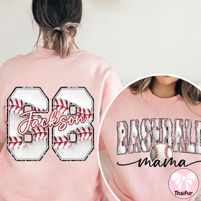 May include: A pale pink sweatshirt with baseball graphics. The left side has the number "68" with "Jackson" in script. The right side shows "Baseball Mama" with a baseball graphic. A ThaiFur logo is at the bottom.