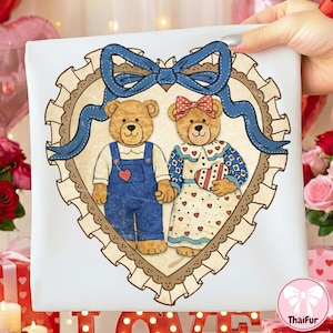 May include: A white square with a heart-shaped design featuring two teddy bears. The bears are within a heart-shaped frame with a blue bow. One bear wears blue dungarees with a heart, the other a dress with hearts.